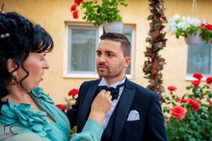 A couple in formal attire shares a tender moment on a garden patio with red flowers in the background.