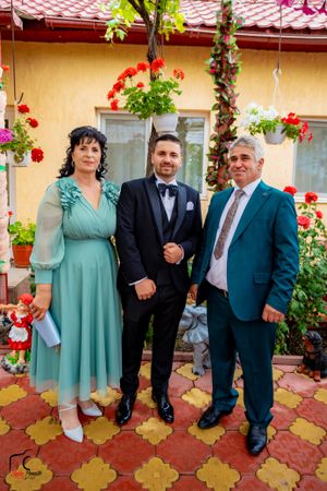 Group photo in formal attire standing against yellow wall with red flowers and decorative tiles.