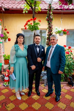 People in formal wear posing on tiled patio with floral decorations and yellow wall backdrop.