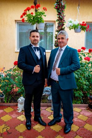 Men in suits giving thumbs up while posing on patterned tile floor near garden.