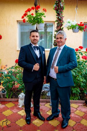Formal group showing thumbs up gestures against yellow wall with red flowering plants.