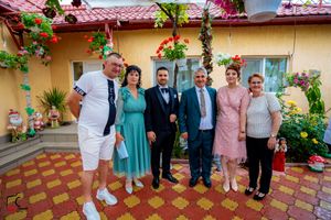 Group photo of wedding guests standing on a decorative tiled patio with flowering plants and yellow walls.