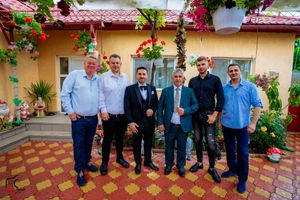 Wedding celebration group photo on outdoor patio with colorful floral decorations.