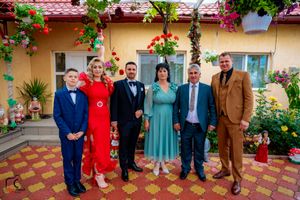 Formal group photo of wedding attendees against yellow wall with red flowers and greenery.