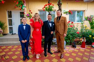 Wedding group photo featuring bright red dress against yellow stucco wall with climbing vines.