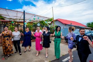 People dancing in a line at an outdoor wedding reception under blue skies.