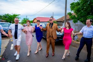A festive group dances together in colorful formal attire on a street during a celebration.