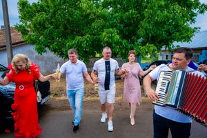 Festive group dances in a line while accordion player provides music on street.