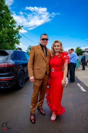 A couple in formal attire stands together against a bright blue sky backdrop.