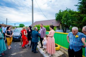 Guests in colorful attire socialize during an outdoor gathering near a bright fence.
