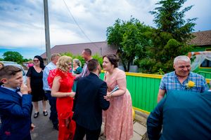 People interact and socialize during a sunny outdoor event near a green fence.