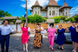People in colorful dresses dancing together on a street with historic buildings and blue sky.