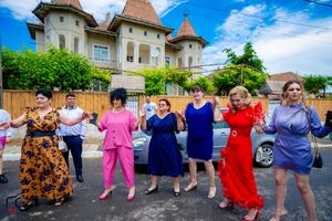 People holding hands in a festive line dance formation against a backdrop of European architecture.