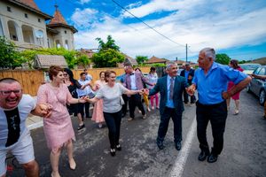 People joining hands in a traditional circle dance on a paved area under bright blue skies.