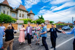 A group of people dancing together in a line on a street with buildings and blue sky in the background.
