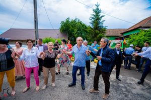 People dancing in a line outdoors at a festive gathering on a sunny day.