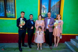 Group photo of people in formal wear standing against a vibrant green wall with yellow window frames.