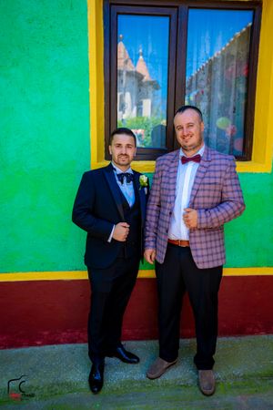 Two people in formal attire pose playfully against a bright green wall with yellow trim.