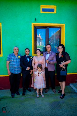 Family members of different ages pose together against a bright green exterior wall.