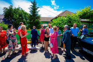 Large group of people gathered outdoors on a sunny day with blue skies and evergreen trees.