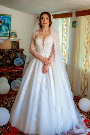 Elegant white ball gown wedding dress with lace details displayed in a sunlit room.