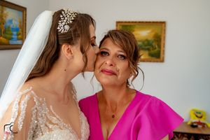 Tender moment captured during wedding preparations in room with landscape paintings.