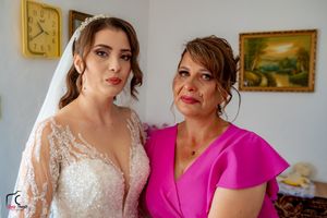 Emotional pre-wedding scene with bride in lace dress and guest wearing bright pink.