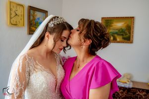 An emotional embrace between two people during a wedding, with framed artwork visible on the wall behind them.