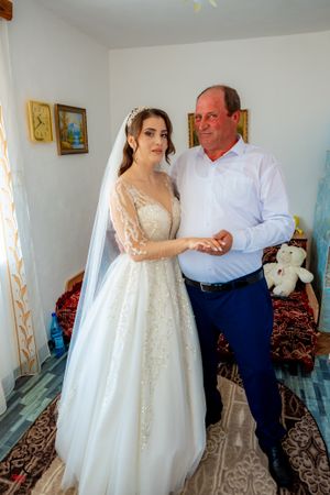 A full-length wedding portrait showing a bride in a sparkly gown with a companion against a simple backdrop.