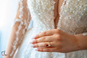 Close-up of a bride's hand showing her delicate engagement ring against her sparkly wedding dress.