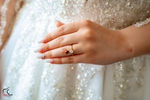 Close-up of perfectly manicured hands displaying an engagement ring against sparkly white fabric.