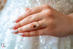 Detailed shot of a manicured hand wearing an elegant engagement ring against a beaded white dress.
