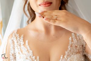 Detail shot of bridal jewelry and lace dress neckline with manicured hands displaying rings.