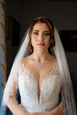 Close-up of bride wearing an intricately beaded white wedding dress with deep v-neckline and sheer veil.