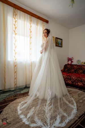 Full-length shot of bride by window showing dramatic cathedral veil with lace detailing.
