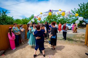 Wide shot of wedding party celebration under decorated archway with balloons.