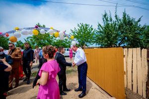 Wedding guests dance and celebrate outdoors on a sunny day with a wooden fence in the background.