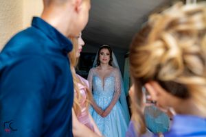 A wedding party gathers indoors wearing blue and pink formal attire.