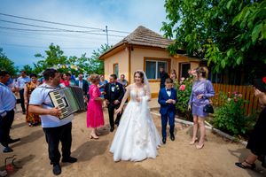 Wedding celebration outdoors with guests gathered on a dirt path near trees and buildings.