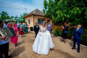 Wedding party and guests walking along a dirt pathway with trees and buildings in background.