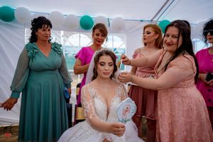 Wedding party members in teal and pink dresses gathered under decorated tent.