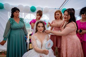 A wedding celebration scene under a white tent with teal balloon decorations and guests in colorful formal attire.