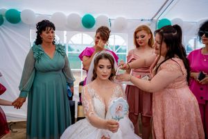 Wedding party members gather under a tent decorated with teal balloons wearing coordinated bridesmaid dresses.
