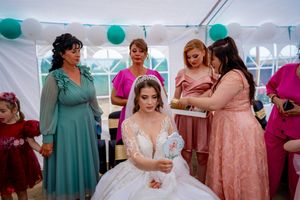 Bridesmaids in various shades of pink and teal dresses celebrate at a wedding reception under a white tent.