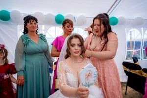 Wedding party members interact during reception under white tent with teal decor and balloons.