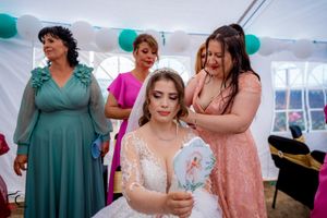 Wedding celebration scene with attendees in formal dresses gathered under decorated white tent.