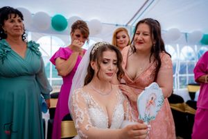 Wedding reception scene showing guests in formal wear under white tent with teal decorations.