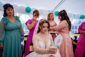 Wedding reception scene showing guests in teal and pink dresses mingling under a white tent with balloons.