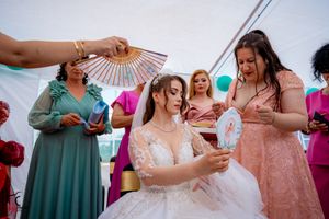 Outdoor wedding reception showing guests in colorful attire mingling under a decorated white tent.