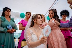 Wedding celebration showing guests in formal wear beneath white tent with teal decorations.